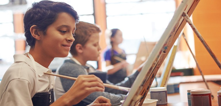 A young boy holds a paintbrush smiling. 